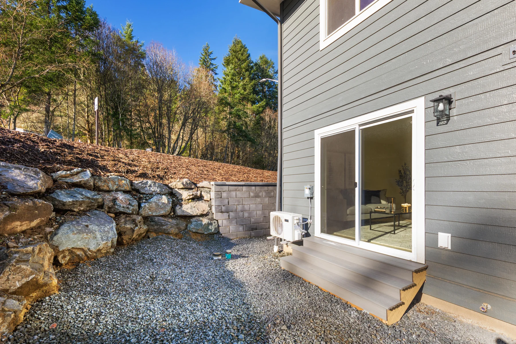 Rear patio beside a townhome with a wooded slope beyond